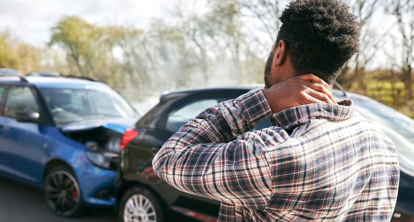 A person holding the back of their neck in pain after a car accident, representing whiplash injury treated at Camrose Physiotherapy.